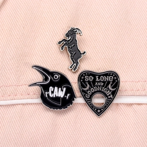 Three-piece black enamel pin set featuring a goat, raven, and a heart-shaped gothic badge