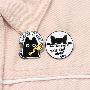 Detail of cute black cat enamel pins with humorous slogans on pink fabric surface