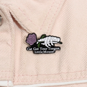 Detail of gothic enamel pin with skeleton hand and purple rose on pink denim fabric