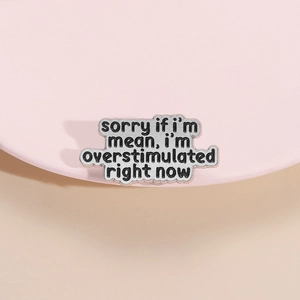 Enamel lapel pin with 'Sorry if I'm mean' text on a pink display stand and beige backdrop