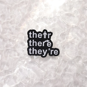 Black enamel pin with Their There They're grammar theme on clear wavy background