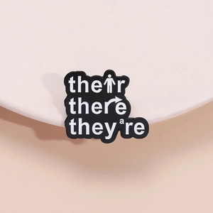 Creative enamel pin featuring their there they are grammar learning puns in black and white