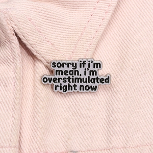 Detail of metal enamel pin with 'sorry if i'm mean' text on pink denim fabric