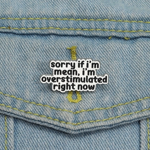 Macro shot of a text enamel pin saying sorry if i'm mean on blue denim fabric background