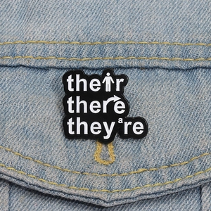 Macro shot of Their There They're grammar enamel pin pinned on a denim jacket pocket