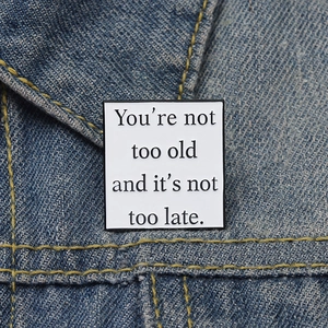 Inspirational square enamel brooch on denim featuring You're not too old quote