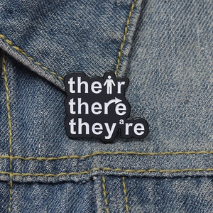 Macro detail of grammar enamel pin on denim jacket featuring their there and they're text