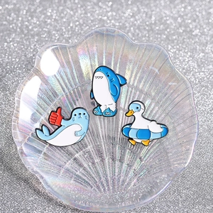 Cartoon animal enamel pins set with blue shark, seal and duck on a shell tray