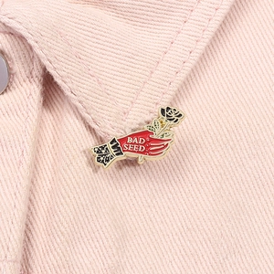 Macro detail of hand holding black rose enamel pin with BAD SEED text on pink denim