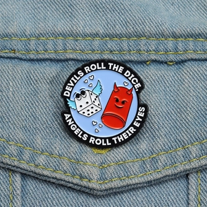 Detail of round enamel pin with devil and dice design on blue denim background