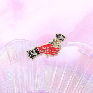 Detailed view of Bad Seed enamel pin featuring a hand holding a black rose flower