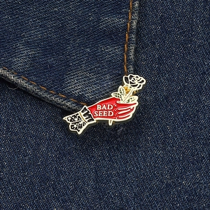 Detailed view of hand and white rose enamel brooch on denim with BAD SEED lettering