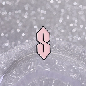 Pink enamel S-shaped badge pin with black outlines on a stylish bokeh background