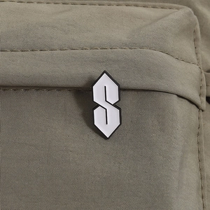 Detail of a black and white enamel Cool S badge pinned on olive green canvas fabric