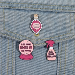 Close-up of pink enamel pins with book themes styled on a blue denim jacket pocket