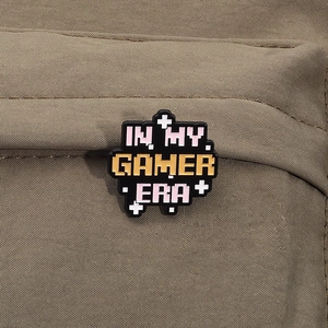 Detail of pixel-style IN MY GAMER ERA enamel pin displayed on a green canvas bag