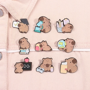 Set of nine cute Capybara enamel pins showing various study poses on pink denim
