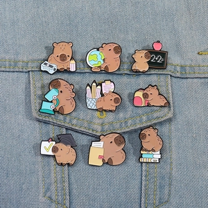 Macro shot of 9 cute educational capybara enamel pins on blue denim fabric background