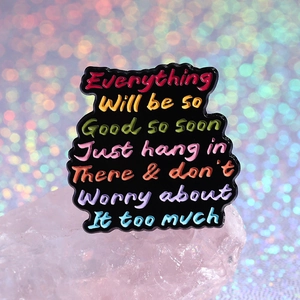 Colorful motivational enamel pin with handwritten text on black background for daily wear