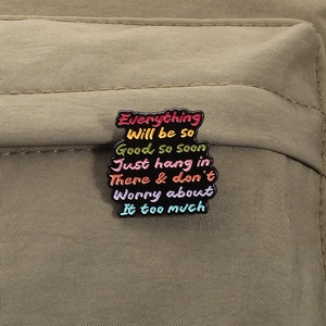 Close-up of a colorful enamel inspirational quote brooch on a khaki canvas fabric texture