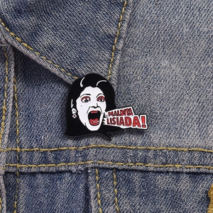 Detailed close-up of a Maldita Lisiada enamel pin styled on blue denim jacket fabric