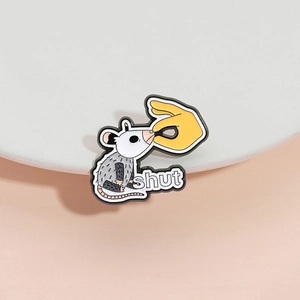White enamel opossum brooch pin with 'shut' text on a minimalist display stand