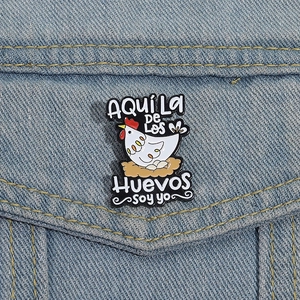 Detail of funny cartoon hen enamel pin on blue denim jacket with Spanish text quote
