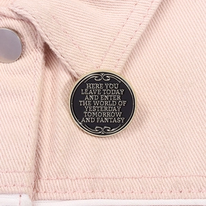Detail of round black enamel pin with golden Disney quote on pink denim fabric
