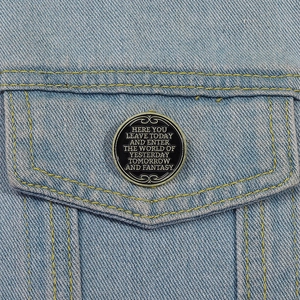 Detail of round enamel pin with gold lettering on a blue denim jacket pocket