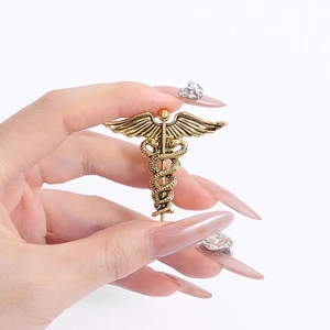 Vintage gold caduceus brooch with double snake and wings design held by hand