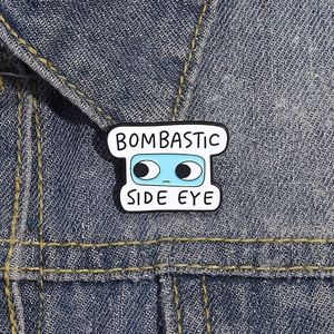 Detailed view of Bombastic Side Eye enamel pin attached to a blue denim collar
