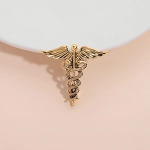 Vintage gold caduceus brooch with angel wings and entwined snakes on a white podium
