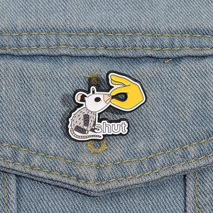 Macro detail of cartoon opossum enamel pin on denim jacket showing 'shut' text design