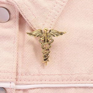 Detailed close-up of a vintage gold Caduceus medical brooch pinned on denim fabric