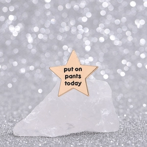 Star-shaped gold enamel brooch featuring black engraved Put On Pants Today text