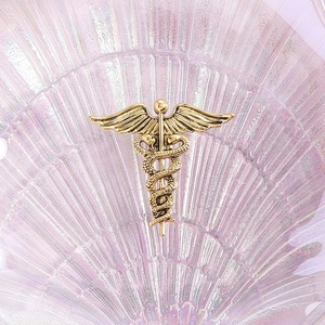 Golden Caduceus brooch with angel wings and snakes on a decorative shell background