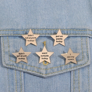 Detail of five gold star pins with funny slogans on a blue denim jacket pocket