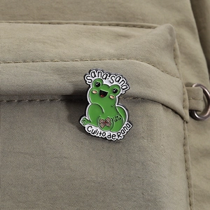 Detail einer grünen Frosch-Emaille-Anstecknadel mit Sana Sana-Text auf Rucksack
