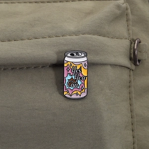 Detail of 'Yes You Can' enamel pin on green canvas showing soda can design and texture