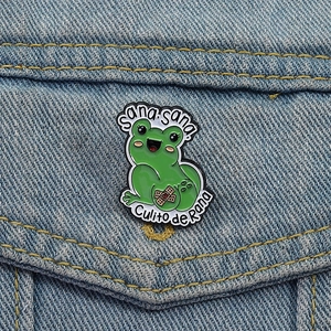 Cute green enamel frog brooch with Sana Sana Culito de Rana text on denim jacket