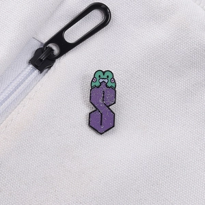 Dettaglio della spilla smaltata viola glitterata a forma di S con rana su tessuto bianco