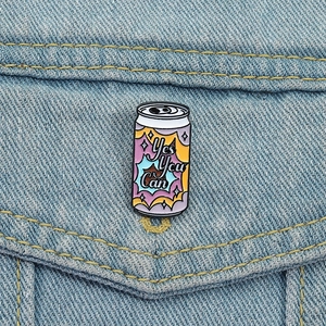 Close-up of Yes You Can soda can enamel pin on blue denim fabric background