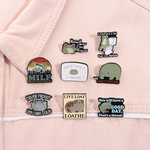 Detail of 8 unique cartoon frog enamel pins with funny phrases on denim fabric