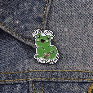 Detail of creative green frog enamel pin with Sana Sana text on denim jacket