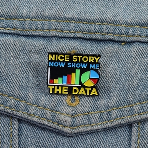 Dettaglio macro della spilla smaltata con grafici dati e slogan su tessuto denim