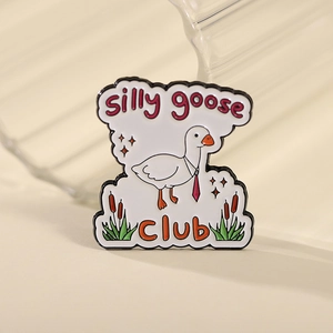 Broche en émail canard blanc avec cravate rouge et texte silly goose CLUB sur fond beige