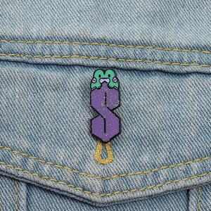 Close-up of a green frog on a purple glitter S-shaped enamel pin on denim jacket