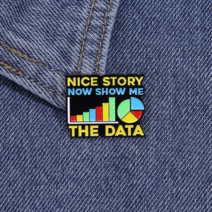 Dettaglio macro della spilla smaltata 'Show me the data' con grafici su denim