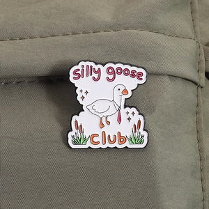Détail macro d'un pin's en émail Silly Goose Club sur une texture de tissu olive foncé