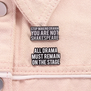 Dettaglio di spille in smalto con slogan Shakespeare su tessuto denim rosa a grana fine
